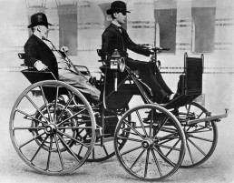 Im Jahr 1886 baut Gottlieb Daimler mit der „Motorkutsche“ sein erstes vierrädriges Automobil. Das Foto zeigt ihn im Fahrzeug, chauffiert von seinem Sohn Adolf.