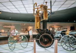 Mercedes-Benz Museum, Raum Mythos 1: Pioniere – die Erfindung des Automobils. Schnell laufender Einzylinder-Viertaktmotor von Gottlieb Daimler, wegen des charakteristischen Aussehens „Standuhr“ genannt. Erstmals wird der Motor in dieser Bauform 1884 verwirklicht. 1885 erfolgt der erste Einsatz im „Reitwagen“, 1886 dann in der „Motorkutsche“, dem ersten vierrädrigen Automobil der Welt.