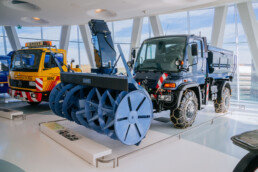 Mercedes-Benz Museum, Raum Collection 3: Galerie der Helfer. Mercedes-Benz Unimog U 500 der Baureihe 405, Winterdienstfahrzeug mit Schneefräse, Schneeketten und Streuaufbau aus dem Jahr 2004. Gesamtansicht von vorn links.