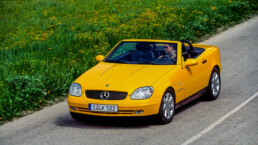 Mercedes-Benz SLK 230 Kompressor der Baureihe R 170 in der Lackierung yellowstone (Mercedes-Benz Farbcode 685). Fahraufnahme mit geöffnetem Verdeck von links vorn aus dem Jahr 1996. (Fotosignatur der Archive von Mercedes-Benz Classic: A96F2372)